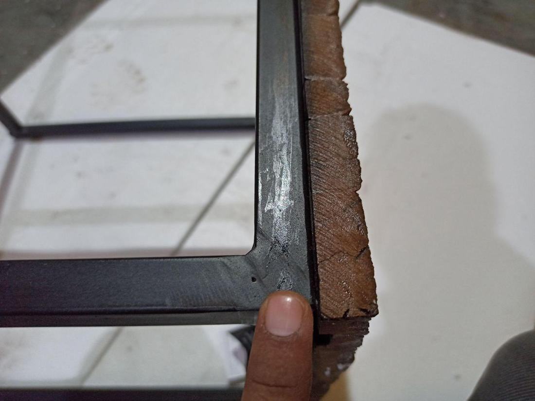 Corner of a black iron frame showing poor ironwork and finish damage, held for the camera at a pre-shipment inspection.