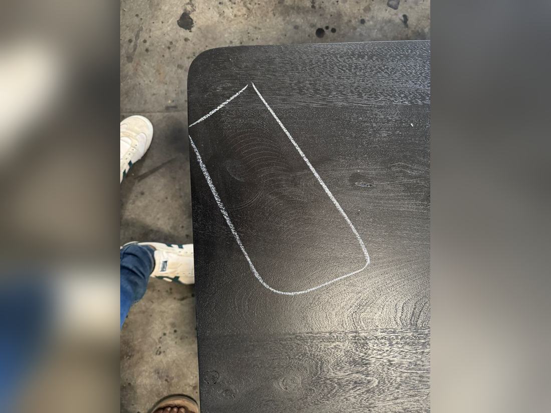 Circular sanding swirl marks showing through a black finish on a solid wood table top, outlined in chalk by the inspector.