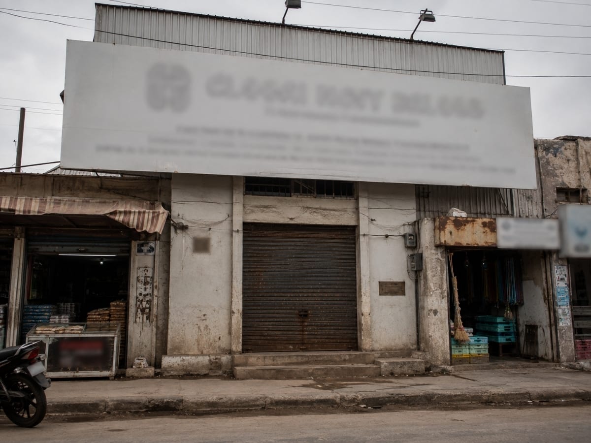 Anonymised street shot: a small locked shutter beneath an oversized "…FURNITURE INDUSTRIES — MANUFACTURER & EXPORTER" signboard, no factory in sight.